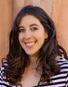 Photo of a smiling white woman with wavy brown hair and blue eyes, wearing a striped dress.