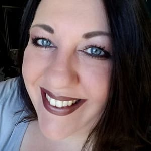 Maria Tureaud, a pale white Irish woman with long, black/brown hair and sapphire eyes smiles at the camera for a head shot.
