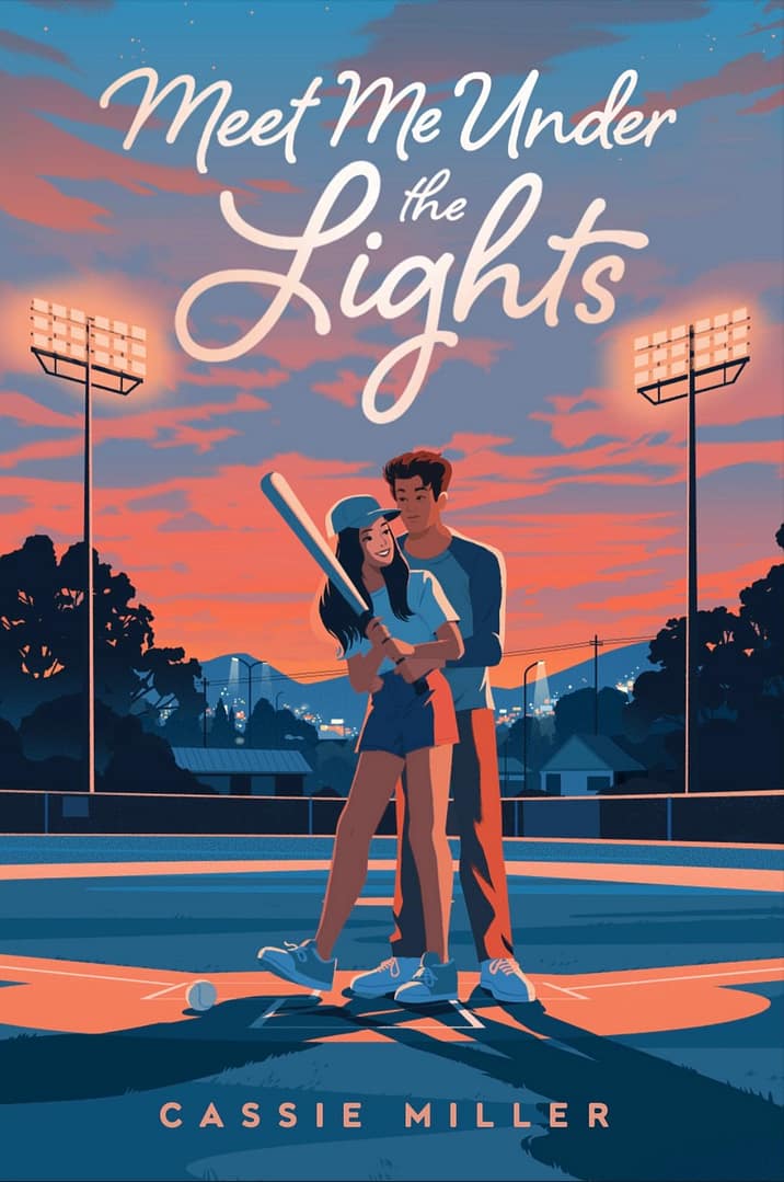 The book cover depicts a sunset of blended pink, blue, and orange behind a small town nestled in the mountains. A teenage girl and boy are featured in the center standing on the home plate of a baseball field, surrounded by the glowing stadium lights. He stands behind her, his hands on her waist as she grips a baseball bat as if ready to take a turn in the box. Both look at each other lovingly. The title is written in loopy white text above the main characters, and the author’s name is written in pink near the bottom of the image.